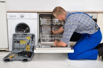 Мастер ремонтирует посудомоечную машину